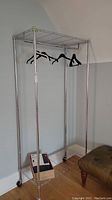 Full front view of metal clothing rack with five hangers and lower shelf with box