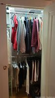 Closet view showing assorted women's tops, jackets, and slacks hanging on racks.