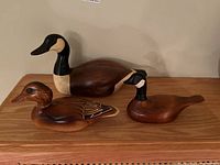 Photo showing all three wooden duck figurines, including one larger Canada goose and two smaller ducks on a wooden surface.