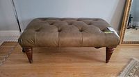 Front view of the tufted leather bench showing button tufting and wooden legs.