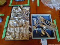 Over 30 pieces of assorted spoons, forks, and teaspoons arranged in trays showing variety in handle designs and sizes.