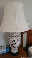 Close front view of one lamp showing white porcelain base with floral pattern and cream shade.