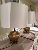 Side view of the pair of brass base table lamps with white drum lampshades set on a wooden surface.