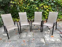 Set of four weathered patio chairs with metal frames and beige woven sling seats and backs, arranged outdoors on stone patio.