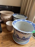 Four ceramic pots displayed on a wooden surface, three are large blue and white patterned planters and one small beige pot.