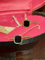 Close-up of one cufflink showing black square stone in gold-tone setting.