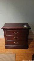 Front view of a dark wooden nightstand with three drawers and metal handles.