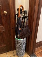 Full view of ceramic umbrella stand filled with umbrellas, canes, and shoehorn.