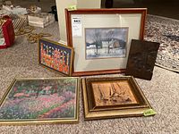 Five pieces of wall art arranged on carpet including the winter barn landscape watercolor, colorful folk art print, floral landscape print, sailboats painting on wood in gold frame, and carved wooden art piece.