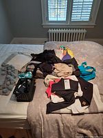 Overview of folded and piled women's clothing items including black leggings, various tops, and a laundry basket with small clothing items