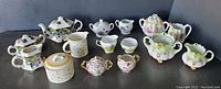 All 21 vintage and antique sugar and creamer containers arranged on a flat surface shows diverse shapes and color patterns