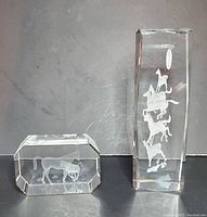 Two 3D glass horse paperweights side by side on black surface, one a horizontal block with a single horse, the other a vertical rectangular prism with four horses stacked inside, lighted stand not included.
