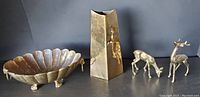 Photo of the four brass items: scalloped bowl with lion head feet, two deer figurines, and tall vase
