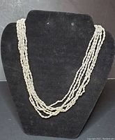 Six-strand freshwater pearl necklace displayed on a black velvet bust showing the texture and layering of pearls.