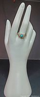 Ring displayed on a hand mannequin, showing full finger fit and overall design with blue teardrop centerpiece and silver filigree band.