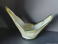 Side view of asymmetrical art glass bowl with yellow, white, and green striping on a black background.