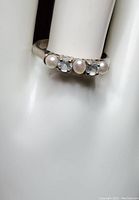 Close-up of sterling silver ring with three white pearls and two clear CZ stones on a holder.