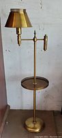 Full view of the mid century brass swing arm floor lamp with built-in tray table, standing against a white wall.