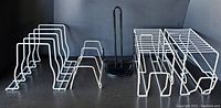 Four metal kitchen organizers: two white can storage racks, one white pan and lid holder, one black paper towel holder on a black background.