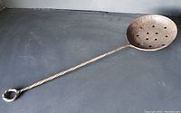 Full view of the cast iron scoop ladle strainer, showing the twisted handle with loop and perforated bowl
