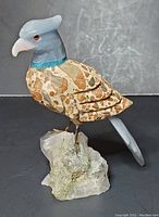 Front and left side view of hand carved hawk figurine on quartz base showing camo patterned wings and blue head with orange eyes.