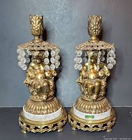 Pair of brass cherub candle holders showing full view, golden brass with hanging crystal prisms, marble base, about 12 inches tall
