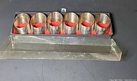 Six Leonard silverplate napkin rings in original worn box with red lining and clear plastic lid visible, showing the full set and box condition.