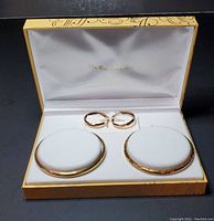 Photo of two gold over sterling silver bangle bracelets and a pair of hoop earrings inside a gift box with white satin lining and gold script logo on the lid interior.
