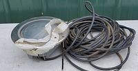 Top-down view of pool light, showing ribbed glass face with partially peeled protective tape and coiled black power cord.