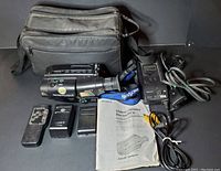 Sony Handycam CCD-TR64 video camera and all included accessories laid out on black surface showing camera, remote, battery charger, power adapter, AV cable, user manual, and carrying case.