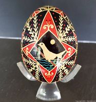 Front view showing the white dove and colorful traditional patterns on the Pysanky egg, displayed on a clear plastic stand.