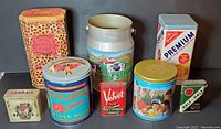 Front view of all eight vintage tins arranged on black background showing various sizes and colorful vintage designs