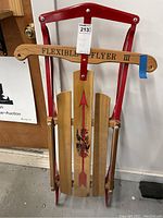 Full front view of the Flexible Flyer III sled showing the wooden slats, red metal frame, and steering bar with printed name.
