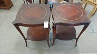 Pair of matching 1920s wooden end tables with leather tops and lower shelves, showing overall condition and shape.