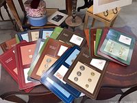 Overview photo of 46 sealed coin sets with various colored folders on a dark wooden surface.