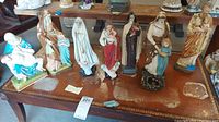 View of seven Catholic religious statues arranged on a table, showing detail, color, and condition including chips