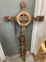 Front view of the entire handcrafted wooden cross with attached chains leaning against a wall.
