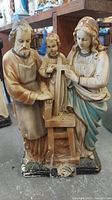 Front view of an antique religious statue depicting Jesus, Mary, and Joseph, showing chips on the base and detailing on clothing and faces.