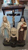 Full view of the Virgin Mary statue, St. Theresa statue, and crucifix on base showing setup and condition