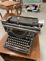 Front view of the black vintage Underwood Standard typewriter showing the brand name and round keys on wooden surface.
