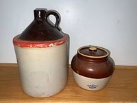 Front view of large stoneware crock and smaller bean pot showing colors, handle, lid, and paint condition