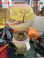 Full view of lamp showing hand-painted glass globe and base with pastoral house, tree, and fence winter scenes, ornate brass base, and electric cord.