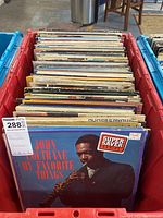Red plastic bin filled with numerous LP records, front visible shows John Coltrane's "My Favorite Things" album cover.