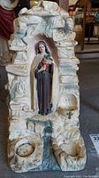 Front view of full religious statue in cave-like niche with stream below