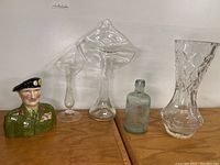 Group shot of all items in the lot: Lord Montgomery portrait jug, two bud vases, vintage bottle, and cut glass vase on wooden surface.