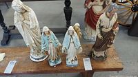Photo showing all five religious statues placed on a wooden bench, with visible chips and flaking on paint surfaces.