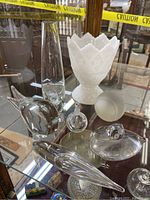 Overview of all items in lot displayed on glass shelf. Includes milk glass vase, multiple glass paperweights of animals, glass stopper, frosted glass ball.