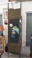 Full view of vintage canvas and metal therapy stretcher standing upright showing entire painted design and structure.