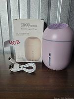 Photo of the light purple bottle-shaped humidifier placed beside its original white box and a USB charging cable on a metal surface.