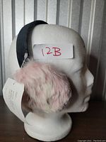 Side view of pink faux fur ear muffs on white mannequin head, showing fluffy texture and black elastic band.